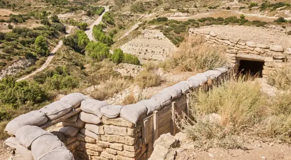 Trincheras de la ruta Orwell, con sacos de arena y un refugio de piedra en un paisaje árido y montañoso.