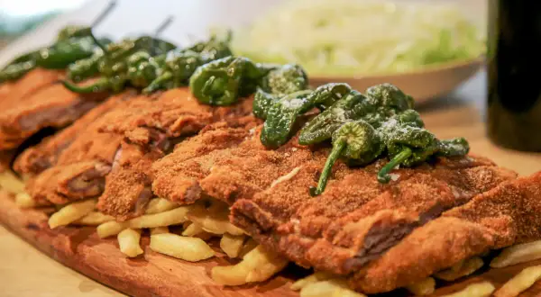 Un festín de cachopo crujiente, patatas fritas doradas y pimientos de Padrón. ¡Una delicia para compartir!
