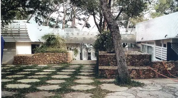 La casa Huarte, rodeada de árboles, presenta un patio con círculos de piedra y césped, muros de piedra y un diseño arquitectónico moderno.