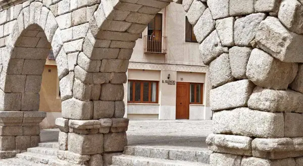 Arcos de piedra del Acueducto de Segovia, un lugar imprescindible que ver en Segovia. Al fondo, la fachada de un edificio con el letrero "El Silencio".