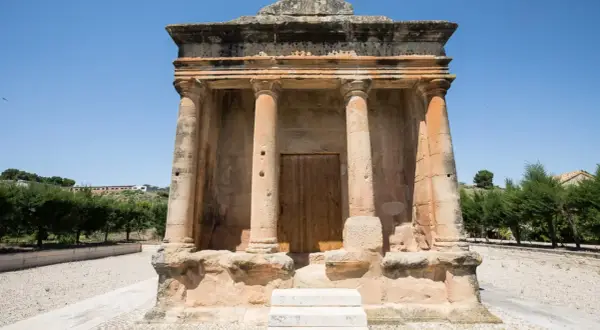 El mausoleo de Fabara, con sus columnas y puerta de madera, se alza imponente bajo un cielo azul.