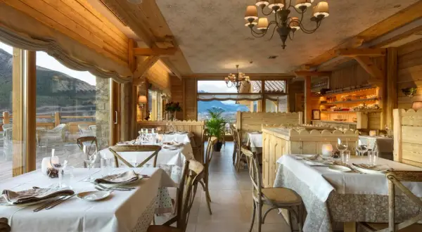 Elegante comedor de madera con mesas puestas, vistas a la montaña. Un lugar perfecto para disfrutar de los restaurantes del Valle de Tena.