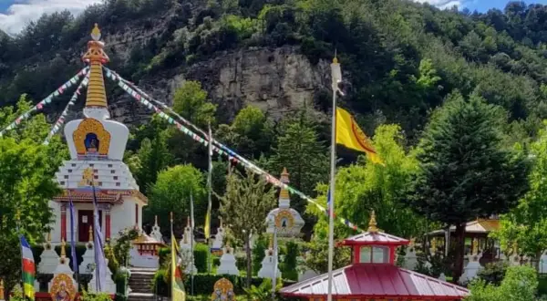 El templo budista Huesca, rodeado de vegetación, con estupas blancas y banderas de oración ondeando.