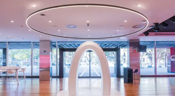Un arco blanco futurista en el centro del espacio Xplora Ibercaja, con una iluminación circular en el techo y grandes ventanales al exterior.
