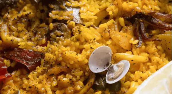 Deliciosa paella en Zaragoza, con arroz amarillo, mejillones, calamares y un toque de limón.