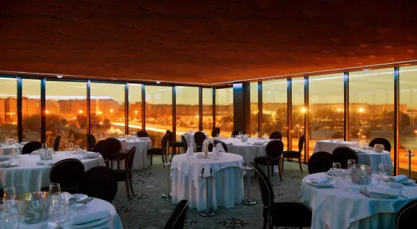 Elegante comedor con mesas puestas y vistas panorámicas de Zaragoza al atardecer. Un lugar perfecto para una cena especial en el rooftop.