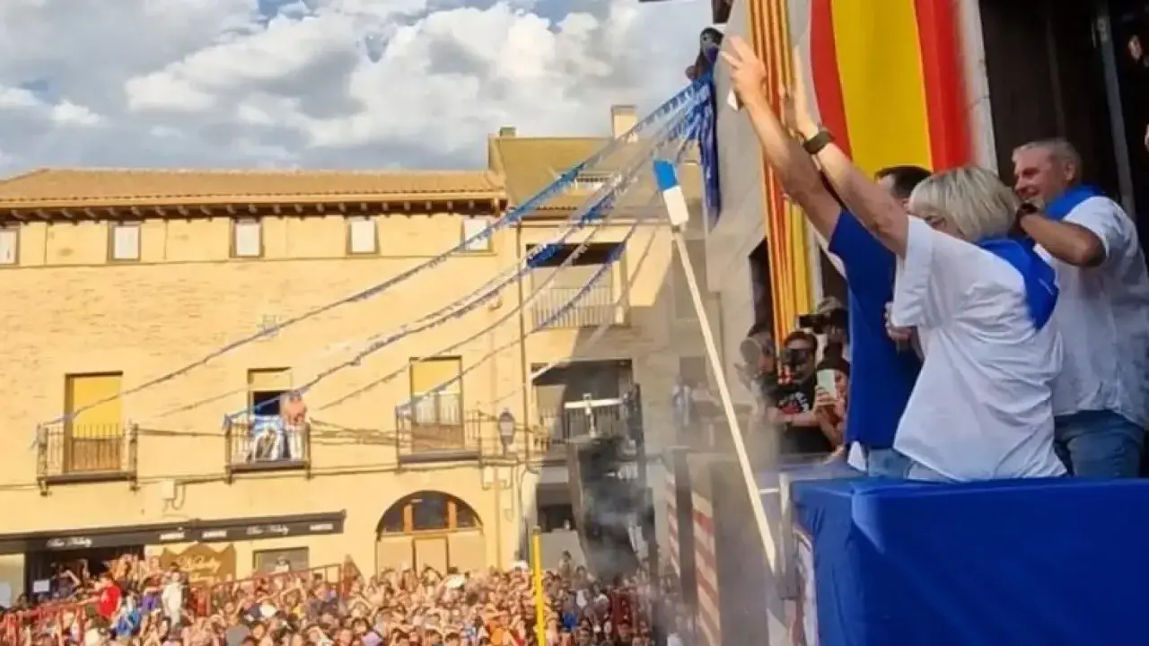 Gente celebra las fiestas de Utebo, ondeando banderas y lanzando confeti desde un balcón.