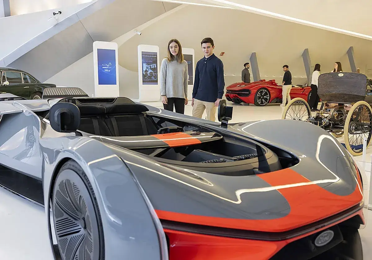 Jóvenes observan coches futuristas y clásicos en una exposición de coches en Zaragoza.