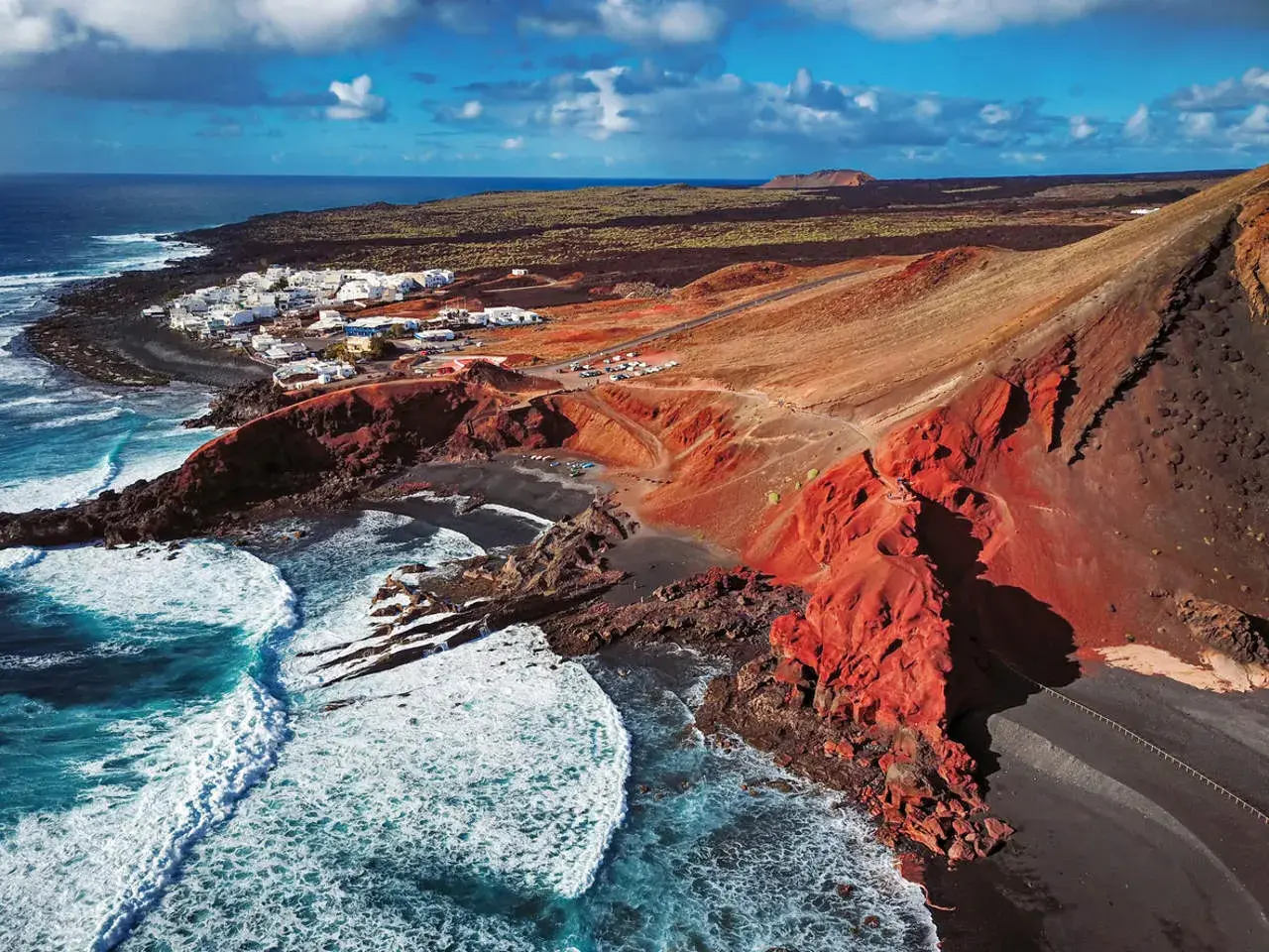Vista aérea de El Golfo, Lanzarote. Un pueblo blanco junto a un cráter volcánico rojo y el mar azul. Imprescindible en tu lista de qué ver en Lanzarote.