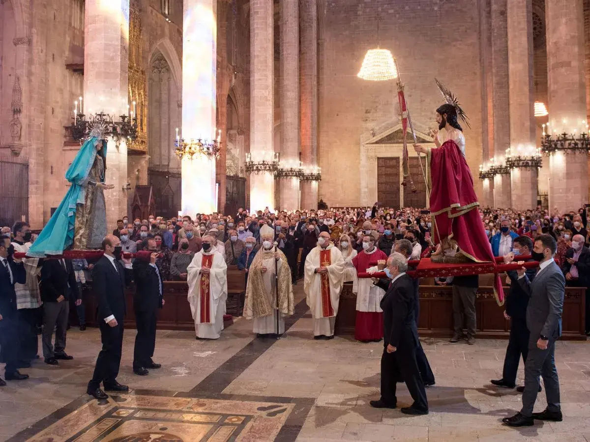 Procesión del Domingo de Resurrección en una catedral. Hombres portan imágenes religiosas mientras fieles observan.