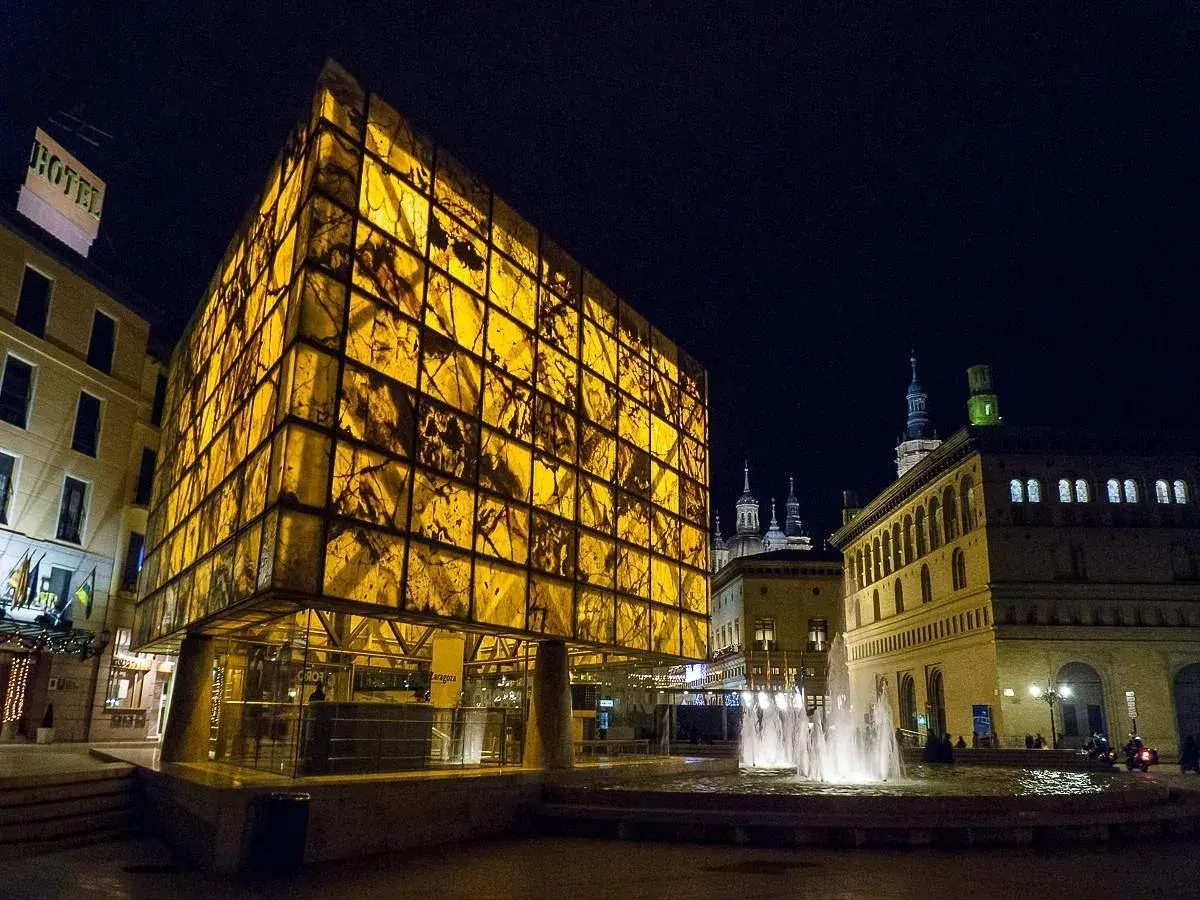 Edificio moderno y translúcido ilumina la noche junto a la fuente, cerca del museo del foro de Caesaraugusta.