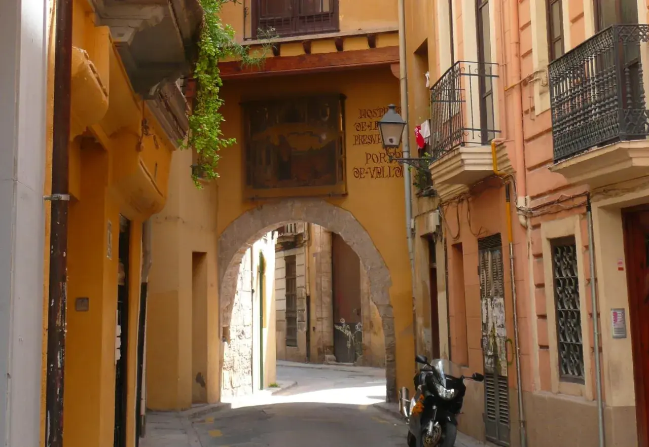 Calle estrecha con arco, fachadas amarillas y naranjas, un balcón y una moto. Descubre los **secret places Valencia**.