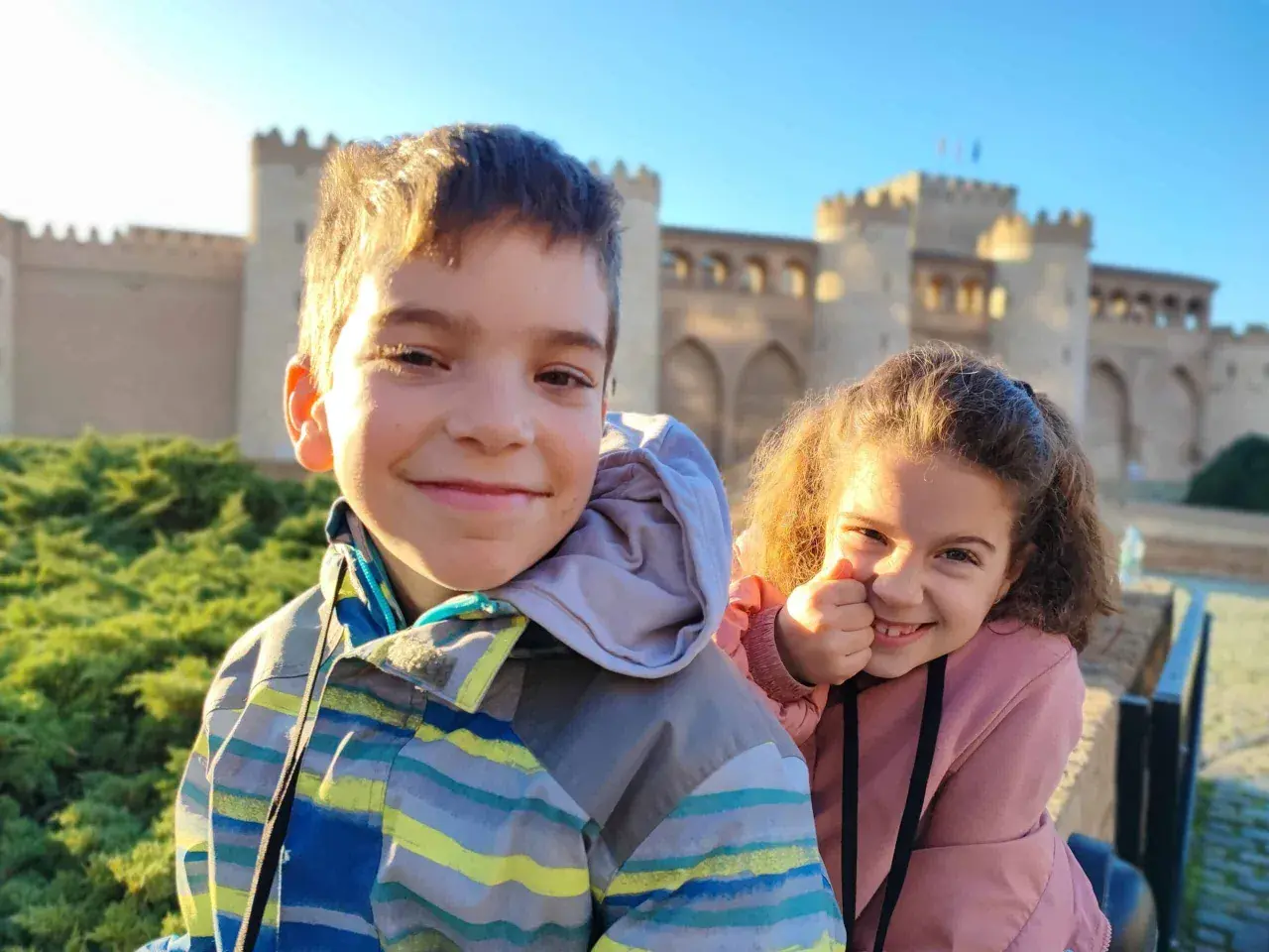 Dos niños sonríen frente a un palacio en Zaragoza. ¡Una aventura familiar en el museo!
