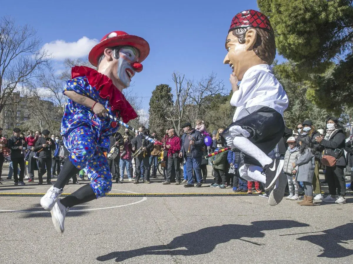 Gigantes y cabezudos saltan en una fiesta popular. Un payaso y un hombre con boina roja celebran el 5 de marzo.