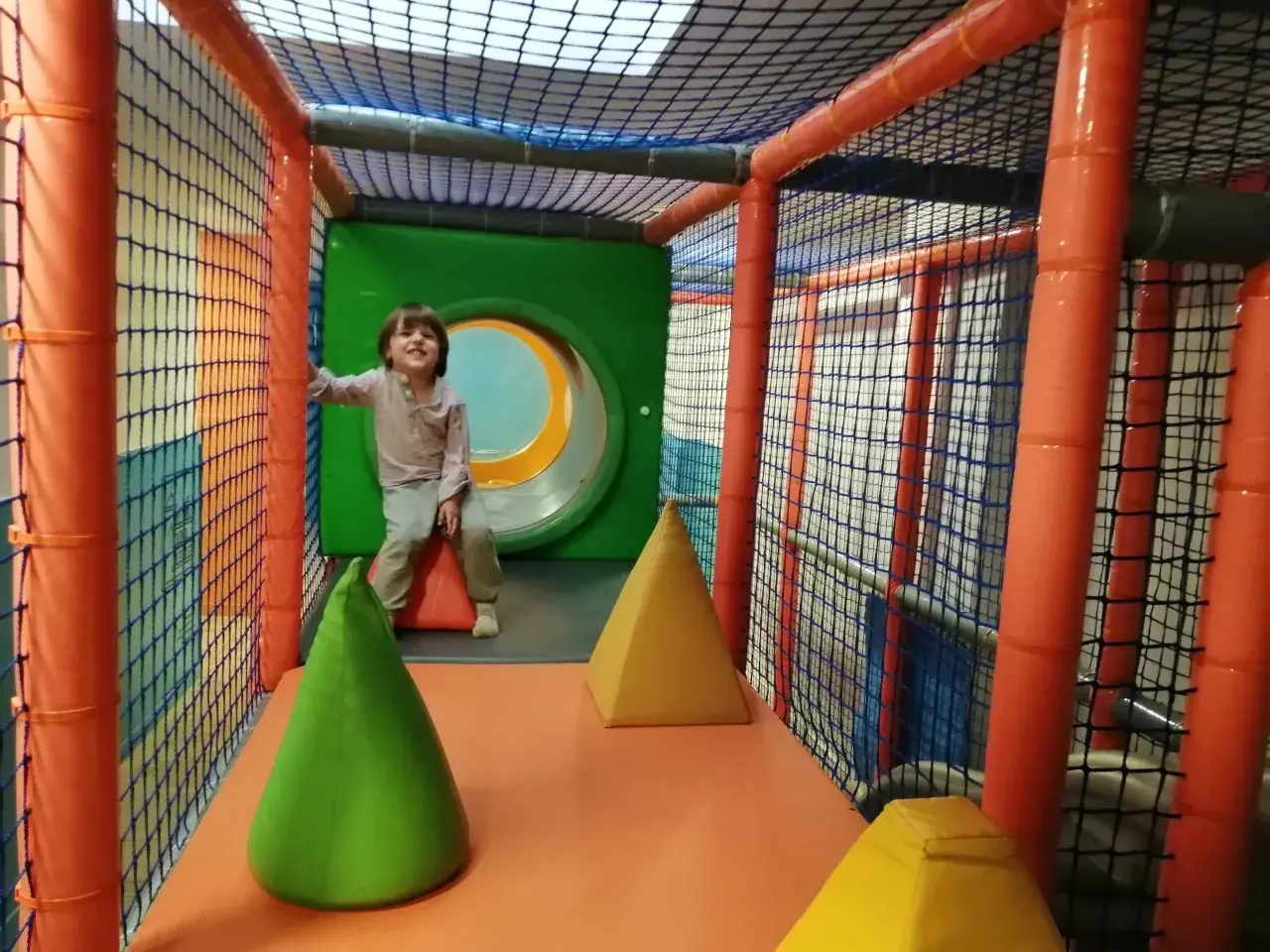 Niño sonriente en un divertido parque de bolas en Zaragoza, rodeado de redes y conos de colores.