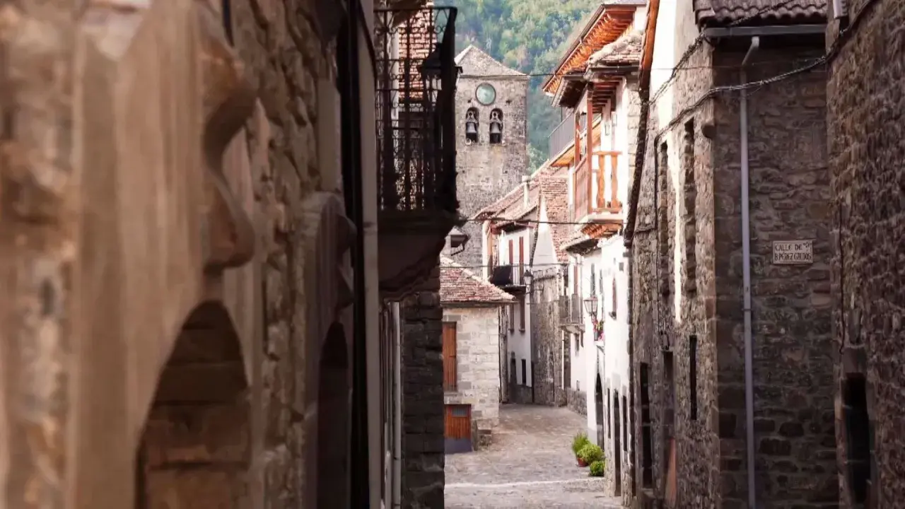 Calle empedrada en un pueblo de Aragón, con casas de piedra y un campanario al fondo.