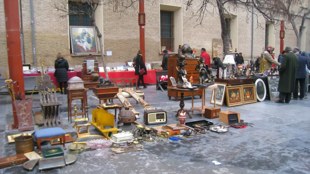 Mercadillo en la plaza San Bruno con antigüedades, muebles y objetos decorativos expuestos en el suelo y mesas.