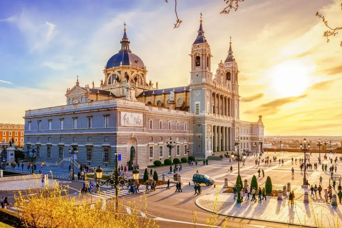 Catedral de la Almudena, uno de los **lugares para conocer en Madrid**, con gente paseando en una tarde soleada.