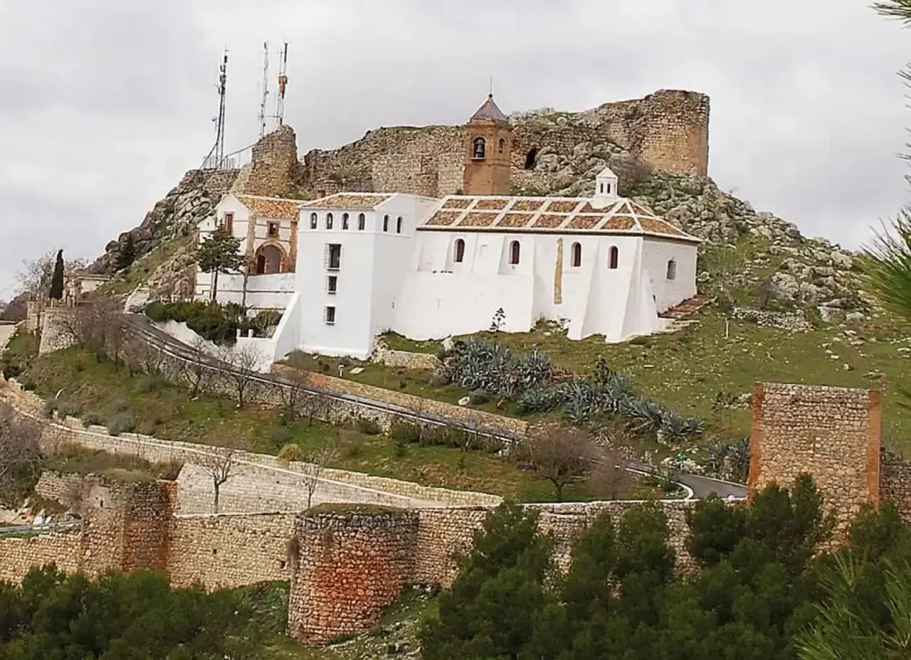 Iglesia Nuestra Señora de Gracia, un edificio blanco con tejado a dos aguas, se alza en una colina rocosa junto a ruinas de un castillo.