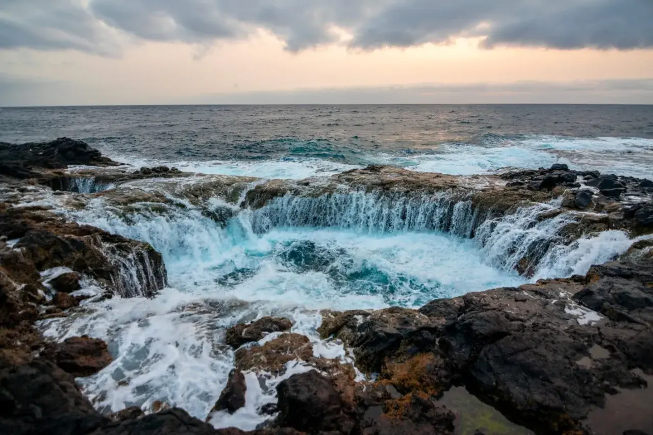 El mar choca contra las rocas volcánicas, creando una cascada de agua azul en un agujero natural. Un lugar impresionante que ver en Gran Canaria.