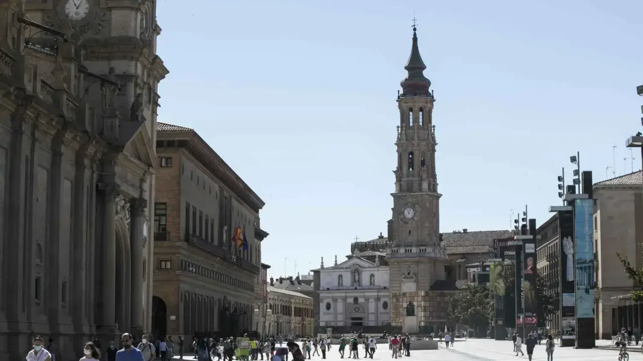 Plaza del Pilar en Zaragoza, con la imponente iglesia de la Seo y el Ayuntamiento. Gente paseando bajo el sol.