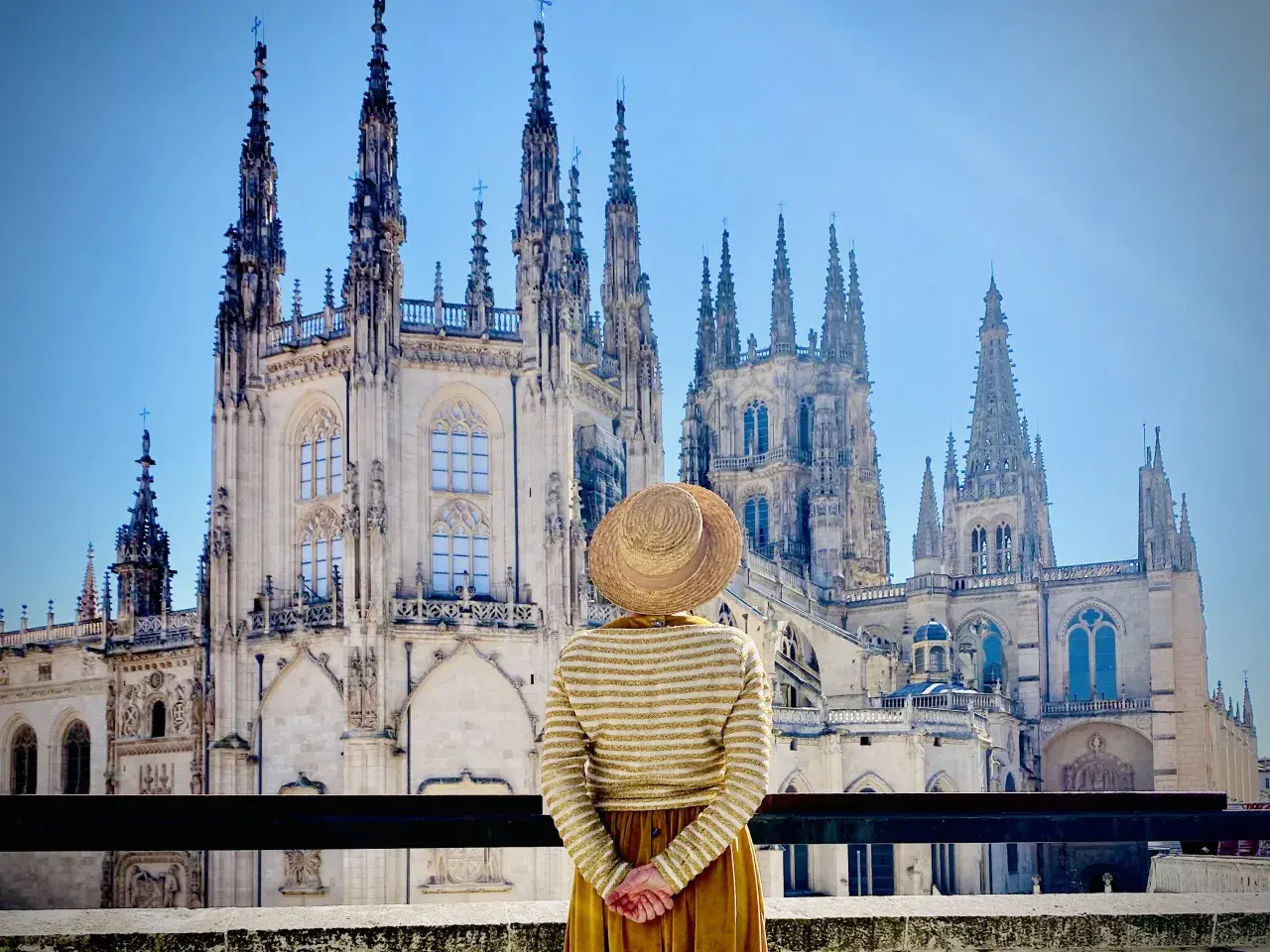Una persona con sombrero admira la majestuosa Catedral de Burgos, considerada por muchos la mejor catedral de España, con sus imponentes agujas y detalles góticos.