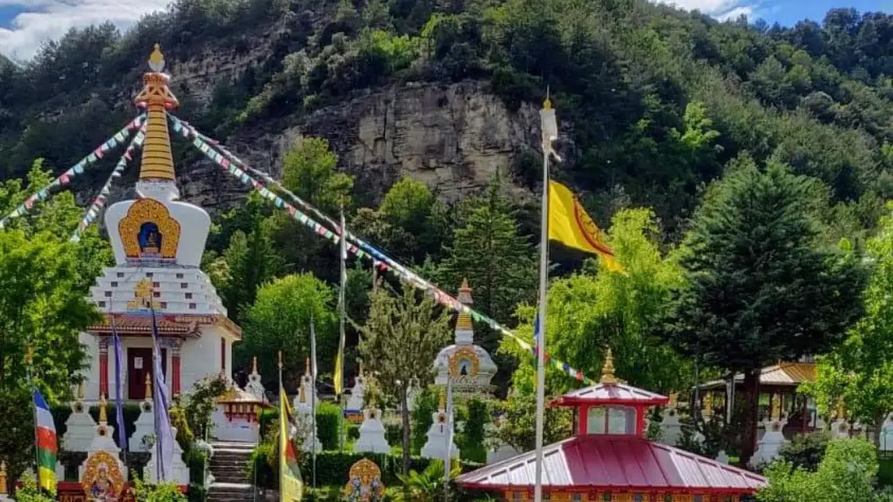 El templo budista Huesca, rodeado de vegetación, con estupas blancas y banderas de oración ondeando.