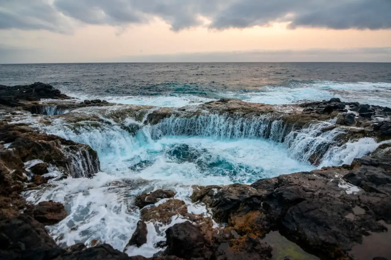 El mar choca contra las rocas volcánicas, creando una cascada de agua azul en un agujero natural. Un lugar impresionante que ver en Gran Canaria.