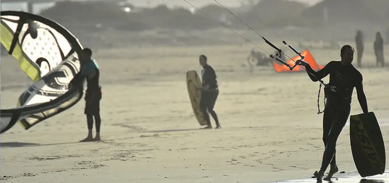 Hombres preparándose para el kitesurf en Lanzarote, con sus cometas y tablas listas para la acción en la playa.