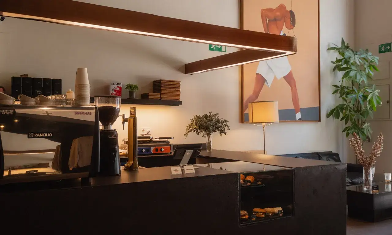 Barra de café con máquina Rancilio, molinillo y grifo de cerveza. En la pared, un cuadro de un boxeador y una planta. Perfecto para un delicioso east crema coffee.