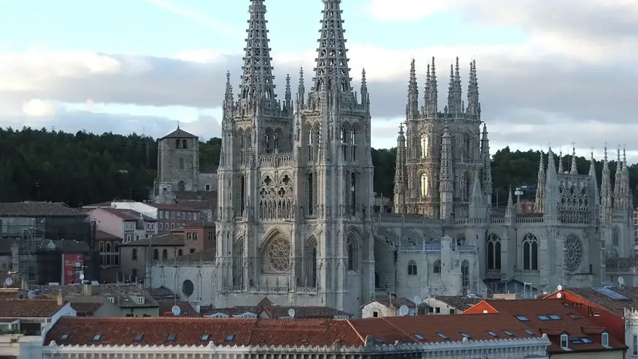 Imponente catedral de Burgos con sus agujas góticas elevándose sobre tejados rojos y un bosque verde.