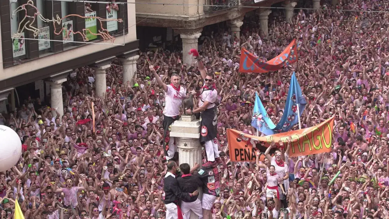 Multitud celebra el programa fiestas Teruel. Banderas y gente vestida de rosa llenan la plaza.