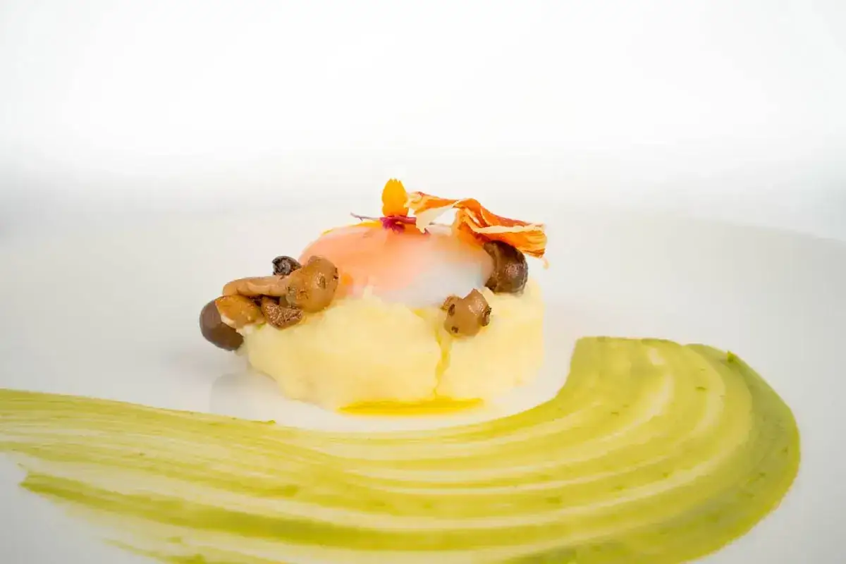Un plato elegante con puré de patatas, huevo escalfado, champiñones y un toque de jamón crujiente. Un entrante perfecto para el menú del Día del Pilar.
