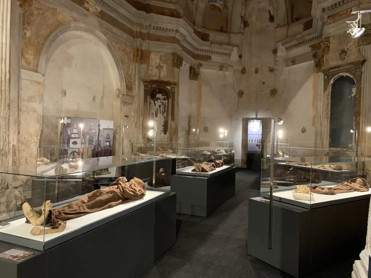 Exhibición de momias en vitrinas en el museo de las momias de Quinto. El interior del museo muestra cuerpos preservados en urnas de cristal, con arquitectura antigua y detalles decorativos en las paredes y techos.