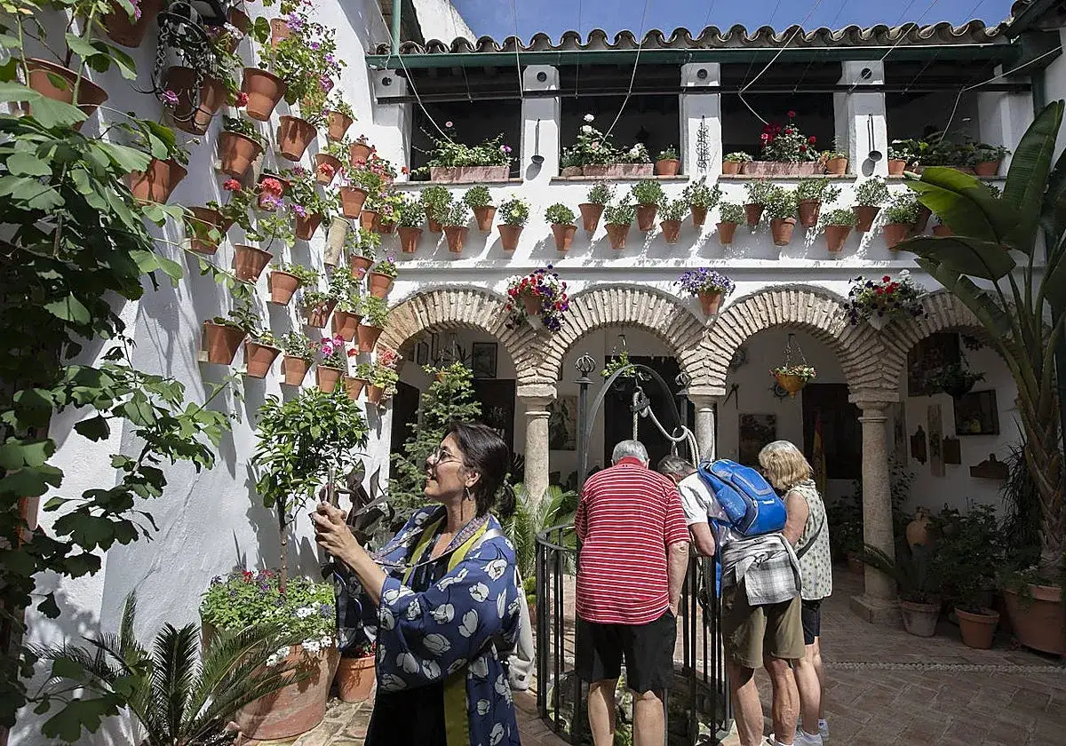 Un patio cordobés, con sus paredes blancas cubiertas de macetas floridas, es lo mejor de Córdoba. Turistas admiran la belleza.