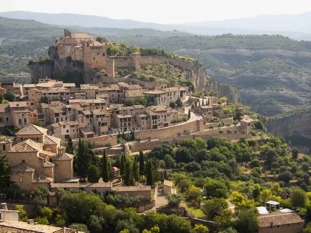 Pueblo medieval en lo alto de un risco, con un castillo imponente. Un ejemplo de las bellas ciudades de Aragón, rodeado de naturaleza verde.