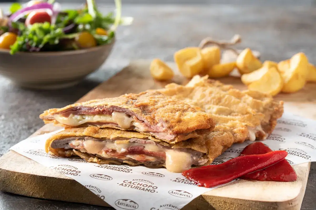 Un delicioso cachopo asturiano, relleno de jamón y queso fundido, acompañado de patatas y pimientos. ¡Un festín para los sentidos!