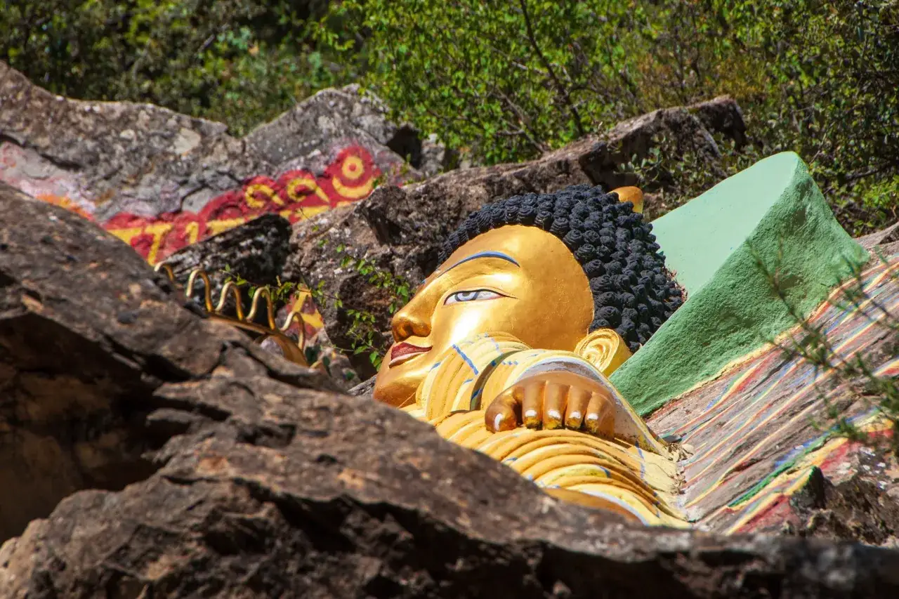 Buda dorado reclinado, parte de un templo budista en Huesca, entre rocas y vegetación.