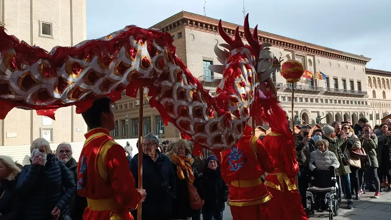 Dragón rojo y dorado desfila en Zaragoza celebrando el año nuevo chino. Multitud observa y toma fotos.