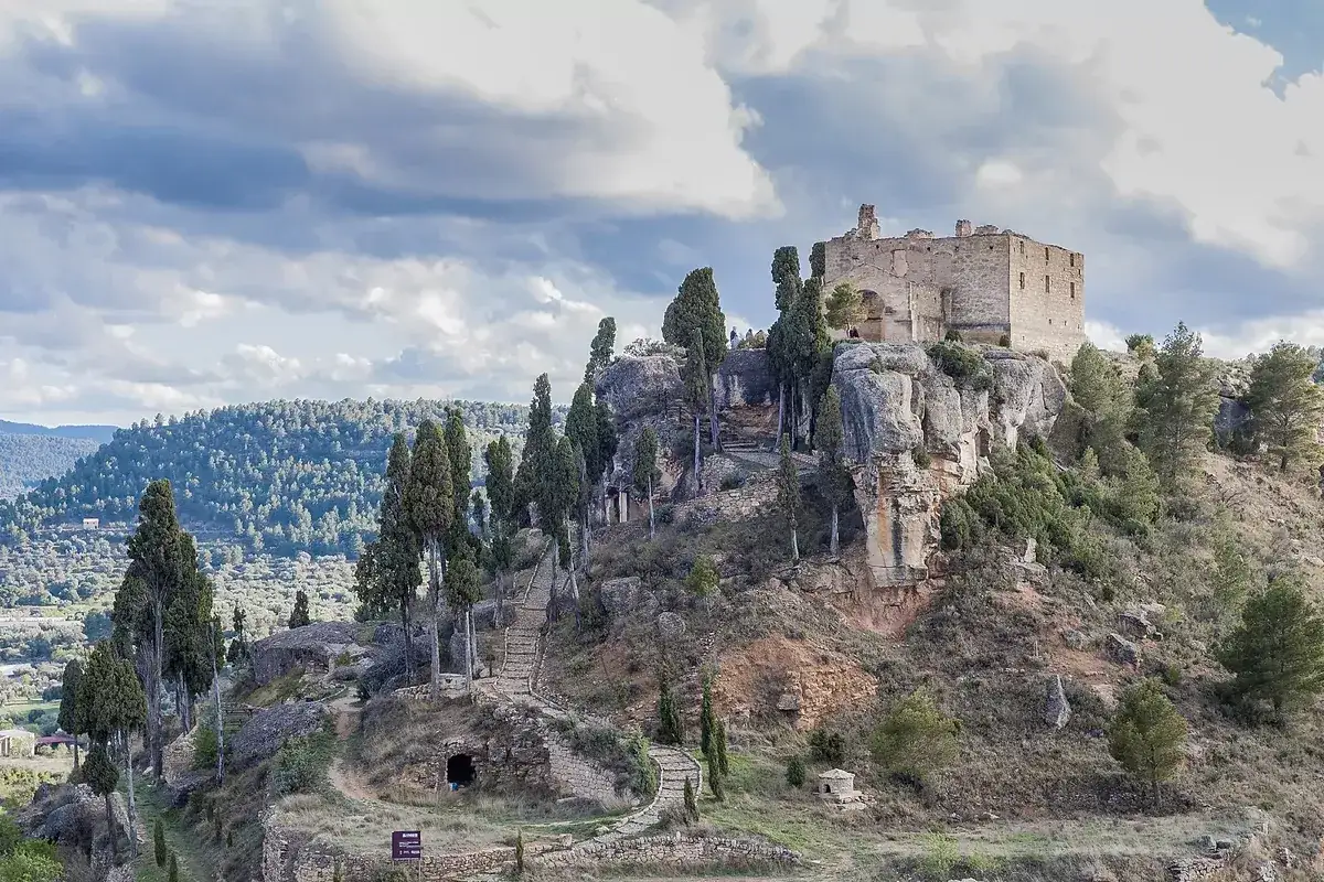 Castillo en ruinas sobre un peñasco, rodeado de cipreses y un camino empedrado. Un lugar con historia, ideal para explorar si buscas qué ver en la fresneda.