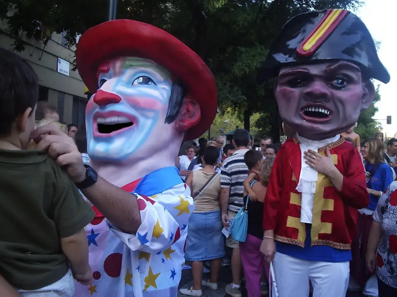 Gigantes con cabezudos delicias, un payaso sonriente y un militar enfadado, desfilan entre la multitud.
