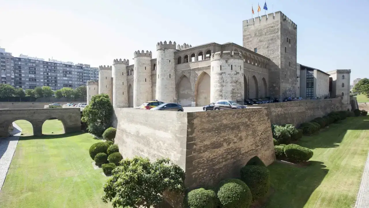 El majestuoso castillo de Zaragoza, con sus torres y murallas de piedra, se alza imponente sobre un césped verde y cuidado.