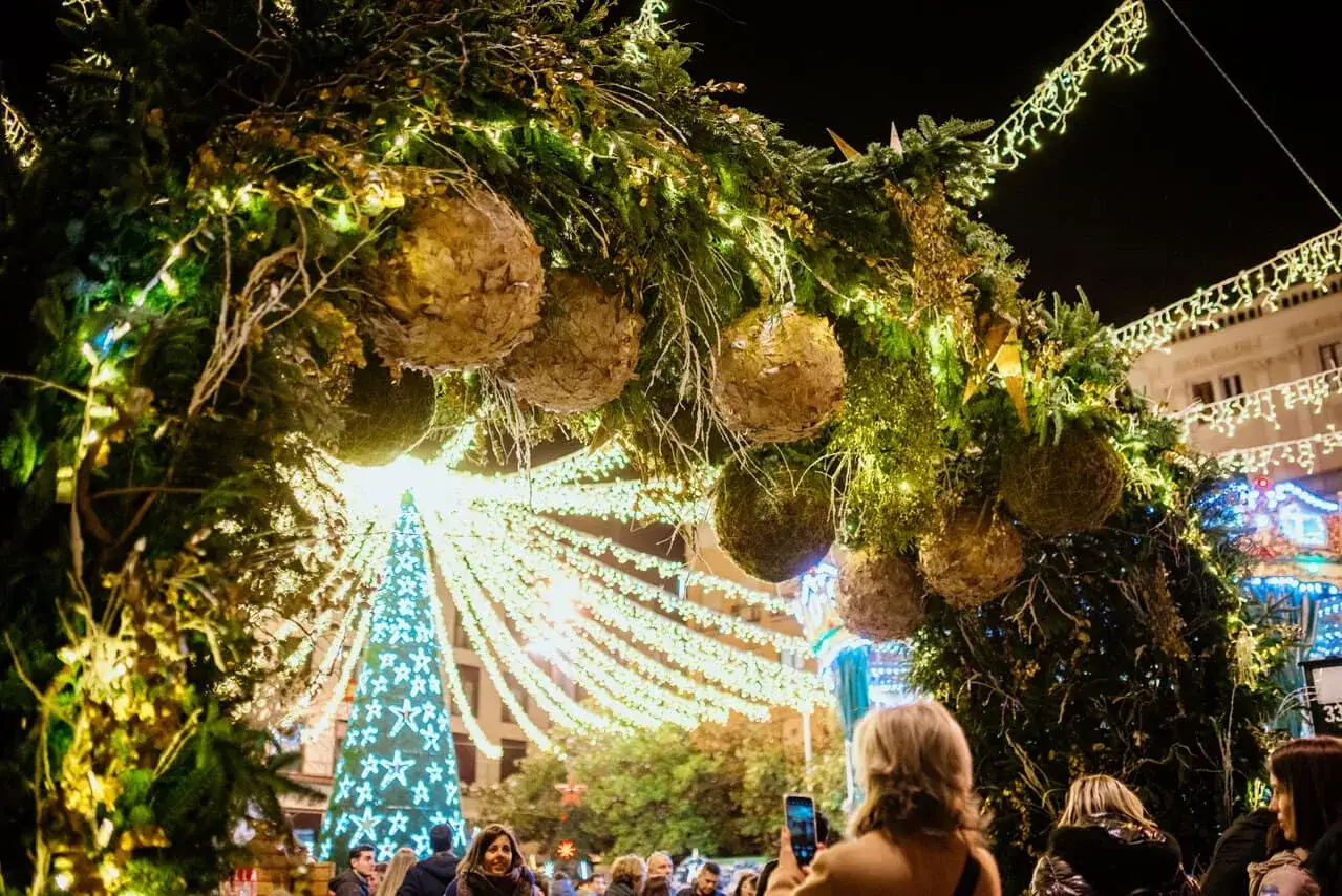 Luces navideñas y un árbol gigante iluminan la noche de Zaragoza. La gente pasea, quizás esperando la llegada de Papa Noel.