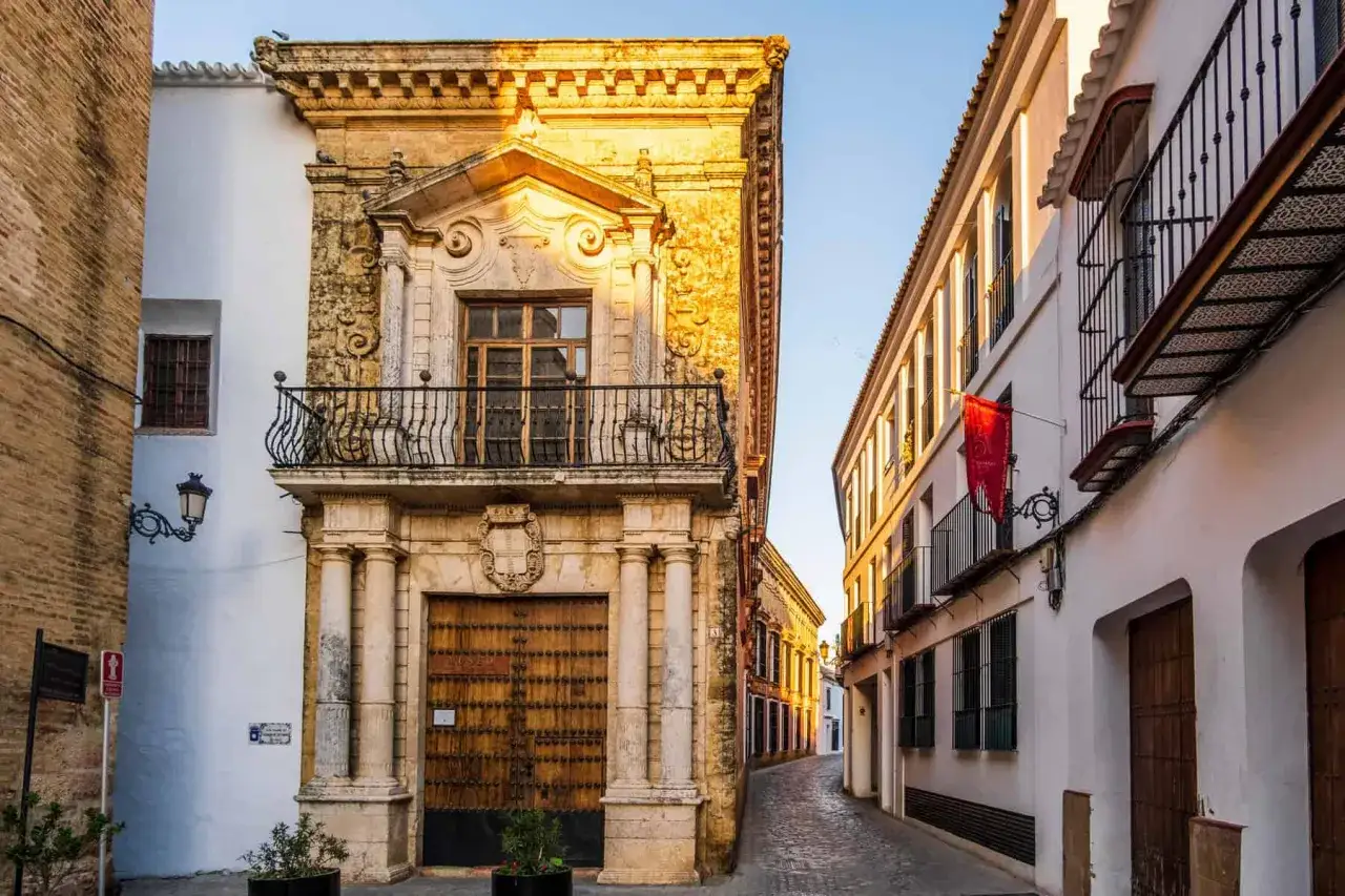 Calle empedrada con edificios históricos, ideal para descubrir qué ver en los alrededores de Sevilla. Fachada de piedra ornamentada y casas blancas con balcones.