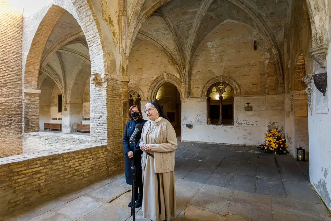 Una canonesa del Santo Sepulcro habla en un claustro histórico, acompañada por otra mujer.