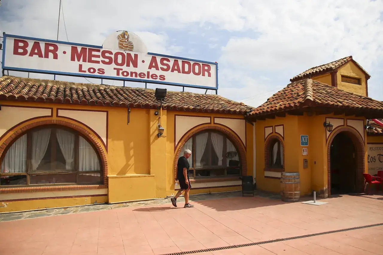 Un hombre camina frente al Bar-Mesón Asador Los Toneles, uno de los restaurantes de Cariñena, con su fachada amarilla y tejado de tejas.