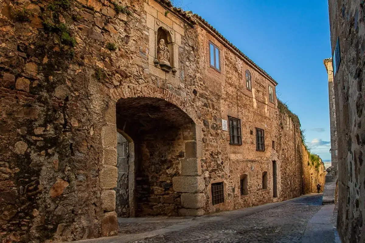 Calle empedrada con arco y nicho con estatua, un ejemplo de qué ver en Cáceres provincia.