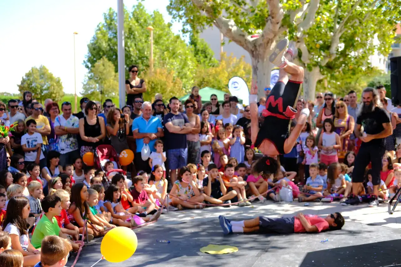 Un acróbata en el aire mientras una multitud mira. Utebo respira circo, con niños sentados y expectantes.