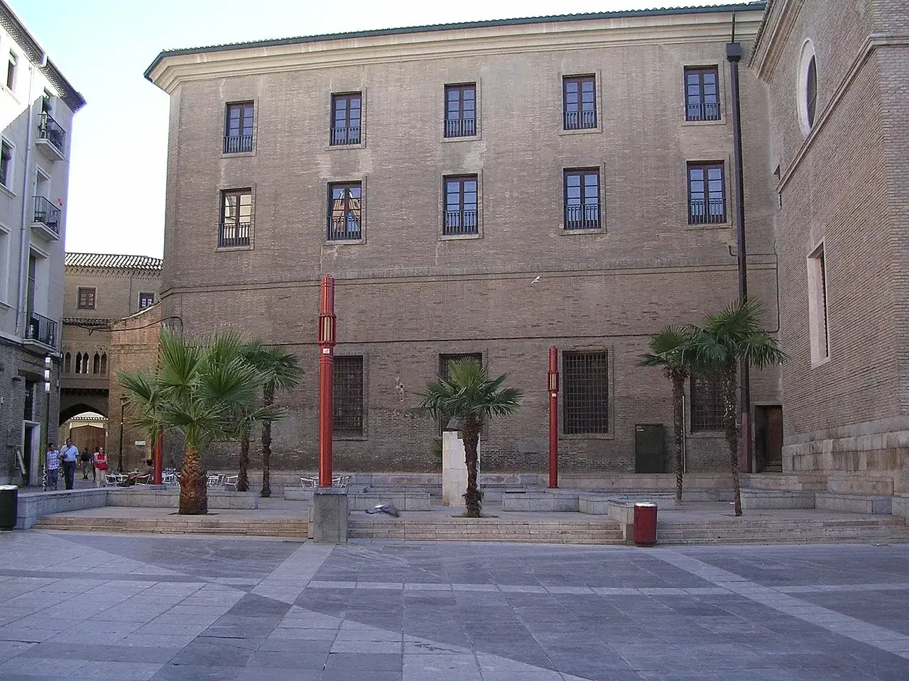 Edificio de ladrillo con palmeras y mobiliario urbano en la plaza San Bruno.