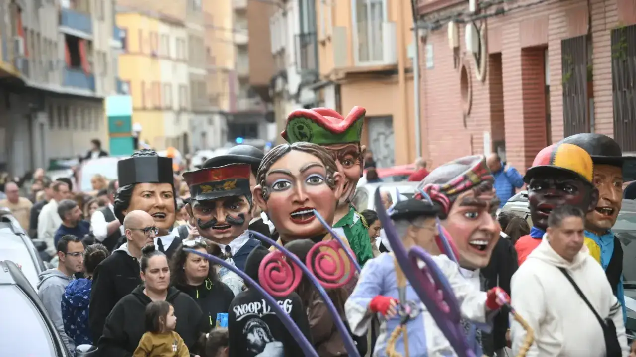 Gigantes y cabezudos desfilan en las fiestas arrabal. La gente observa la colorida procesión en una calle estrecha.